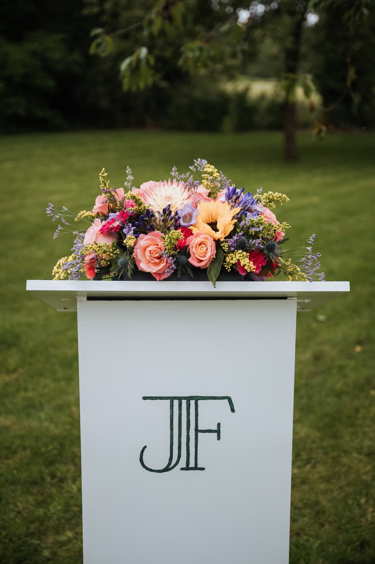 Kleurrijk bloemstuk op een witte ceremoniezuil met monogram