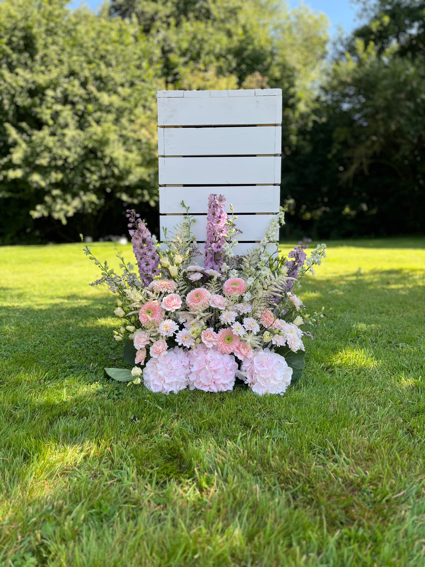 Pastelkleurig bloemstuk in het gras bij een witte zuil
