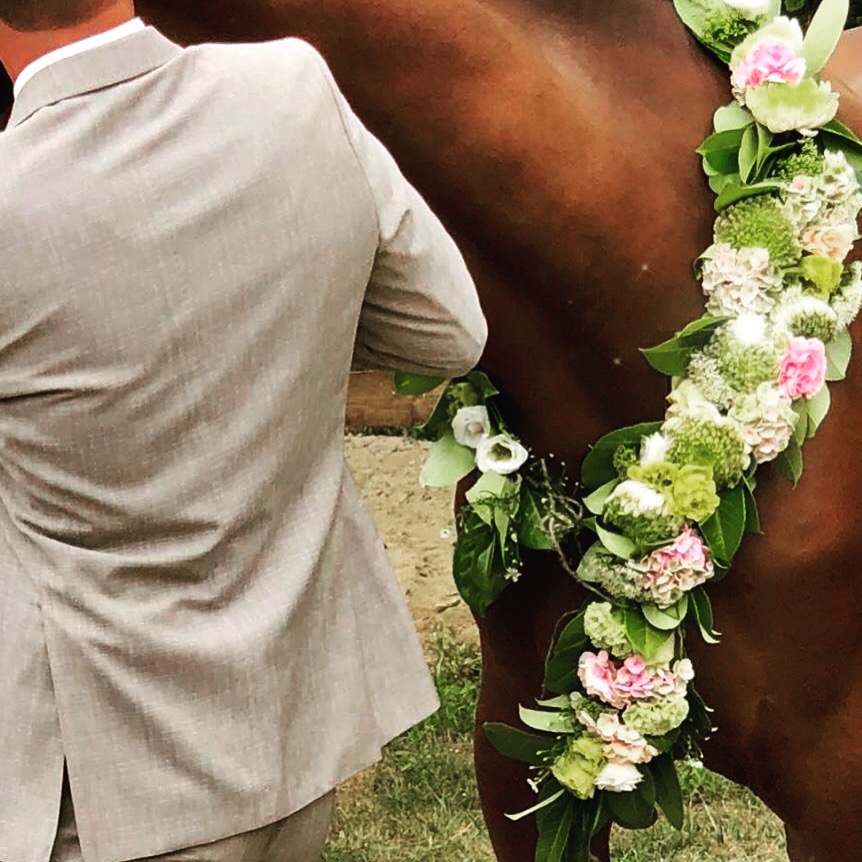 Bloemenkrans in roze en groen rond de hals van een paard