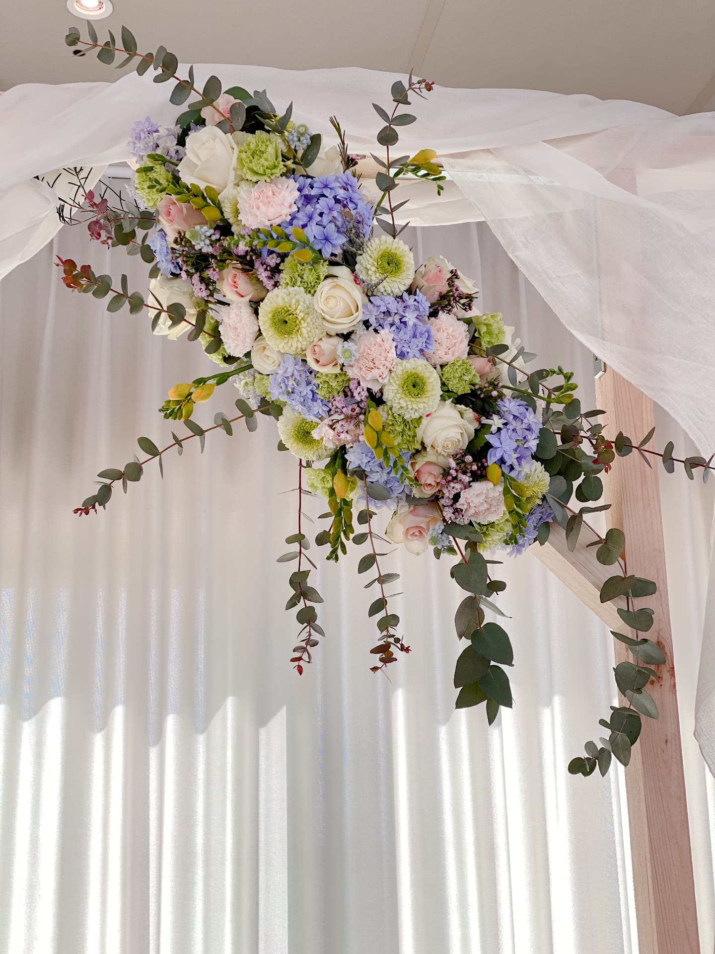 Pastelkleurig bloemstuk op een ceremonieboog met witte voile