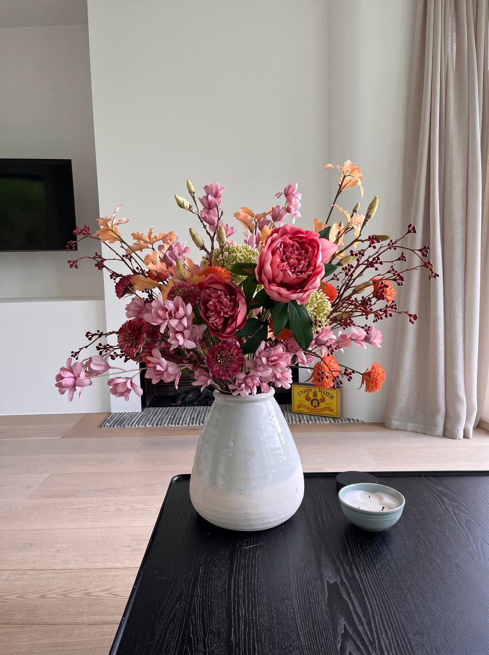 Kleurrijk boeket in een lichtgrijze vaas op een zwarte tafel in een woonkamer