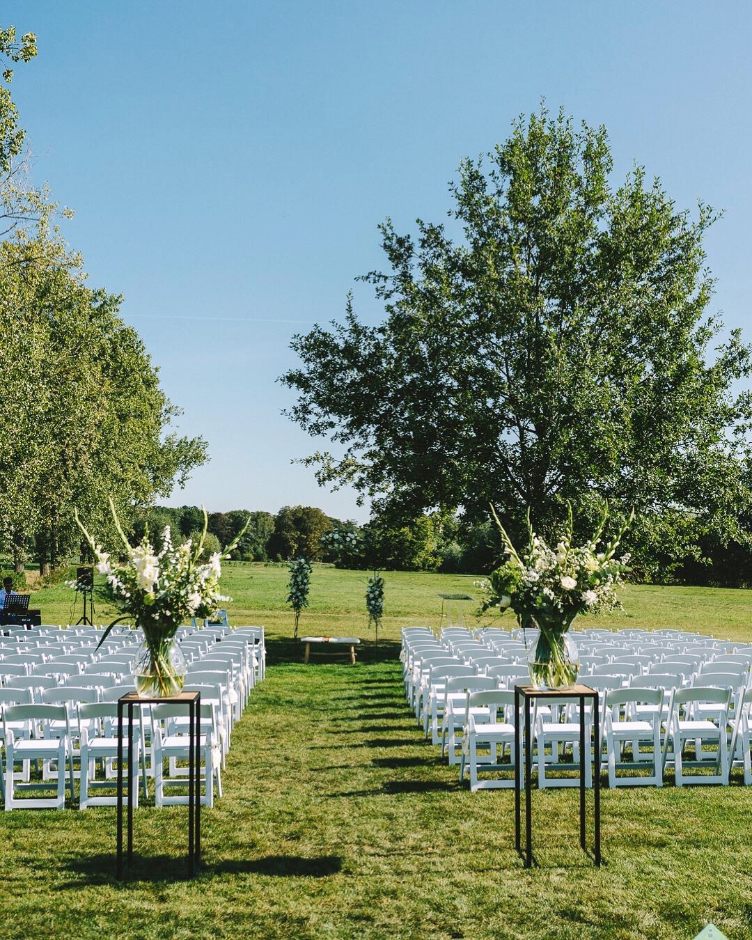 Outdoor trouwceremonie in een groene tuin met witte stoelen en bloemstukken